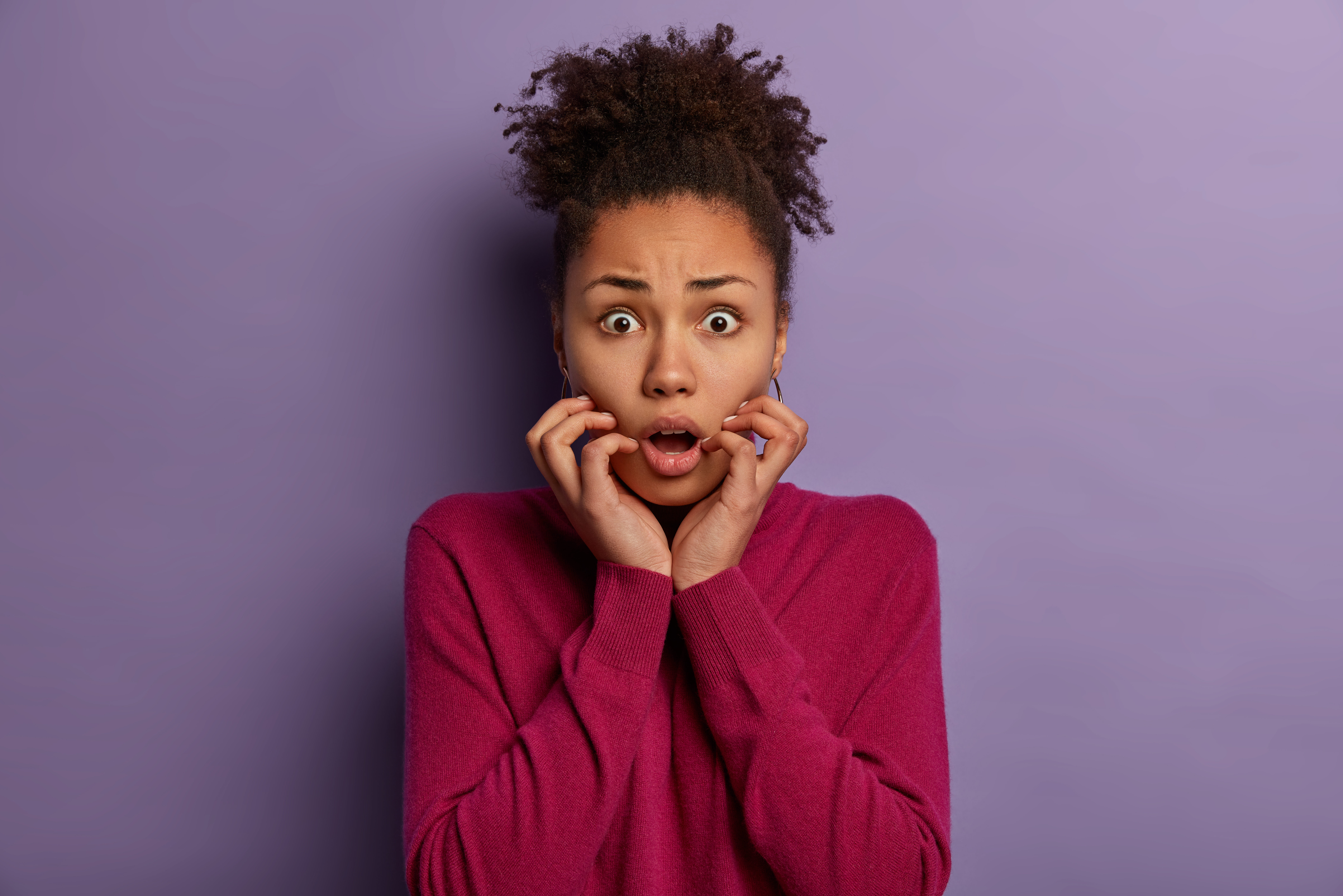 Femme métisse au pull rouge qui a peur sur fond mauve